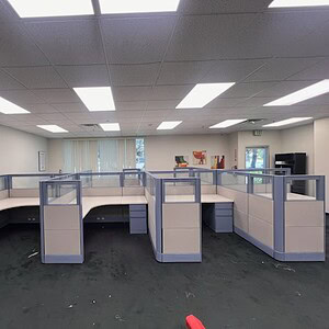 Open office space with cubicles featuring glass partitions and white desks.