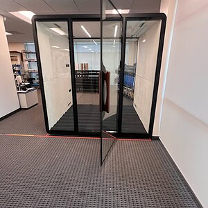 Black-framed glass privacy pod in office space with open door.
