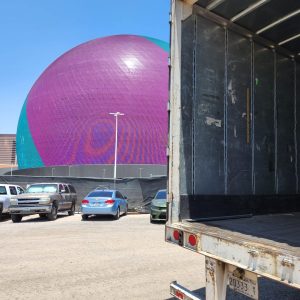 Large purple geodesic dome with parking lot and trucks nearby, showcasing Cube World USA shipping se.