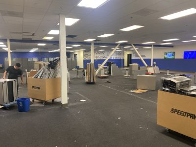 Office furniture liquidation with damaged desks and chairs in a large, empty showroom.