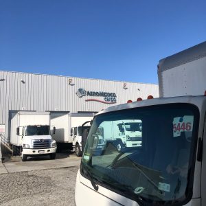 Commercial trucks at Cube World USA shipping facility under clear blue sky.