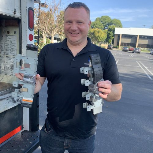 Commercial equipment technician holding electrical components outside.