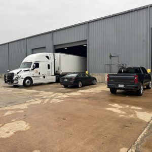 Large semi-truck and vehicles outside warehouse for shipping services.
