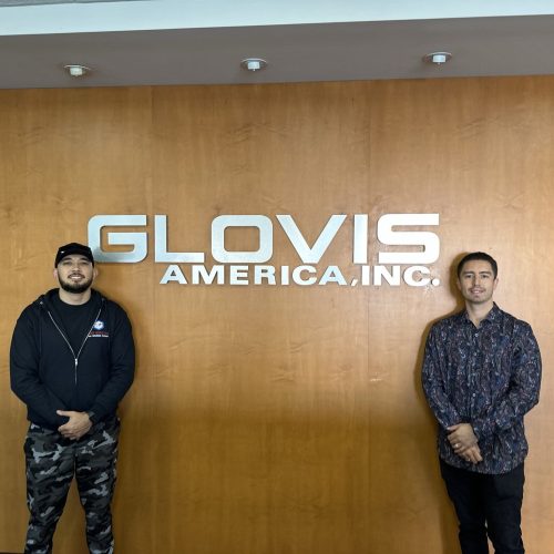 Two men standing in front of Glovis America Inc. sign at Cube World USA office.