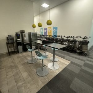 Office break room with tables, chairs, and coffee machines for employee comfort.