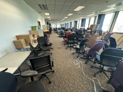 Office furniture liquidation with chairs, desks, and cubicles in a spacious, well-lit room.