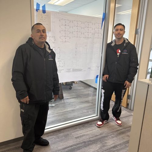Two commercial brokers standing by a glass door with a blueprint in the office.