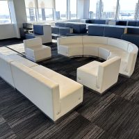 Modern office lounge with white curved seating and large windows.