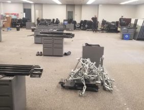 Office furniture liquidation with desks, chairs, and equipment in a spacious warehouse.