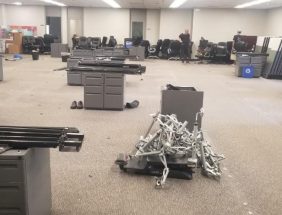 Office furniture liquidation with desks, chairs, and equipment in a spacious warehouse.
