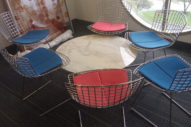 Stylish office meeting space with vibrant chairs and a round marble table near large window.