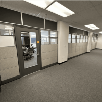 Modern office interior with glass door, cubicle walls, and carpeted flooring.